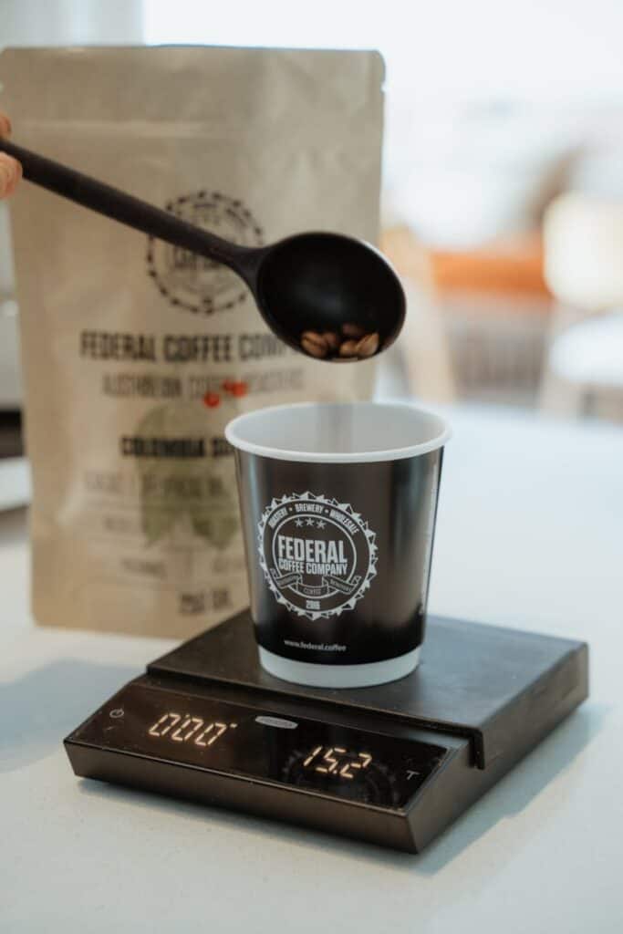 Coffee beans being carefully measured into a cup using a digital scale, focusing on precise brewing.