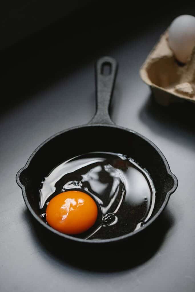 Raw egg in cast iron skillet with eggshells on kitchen counter.