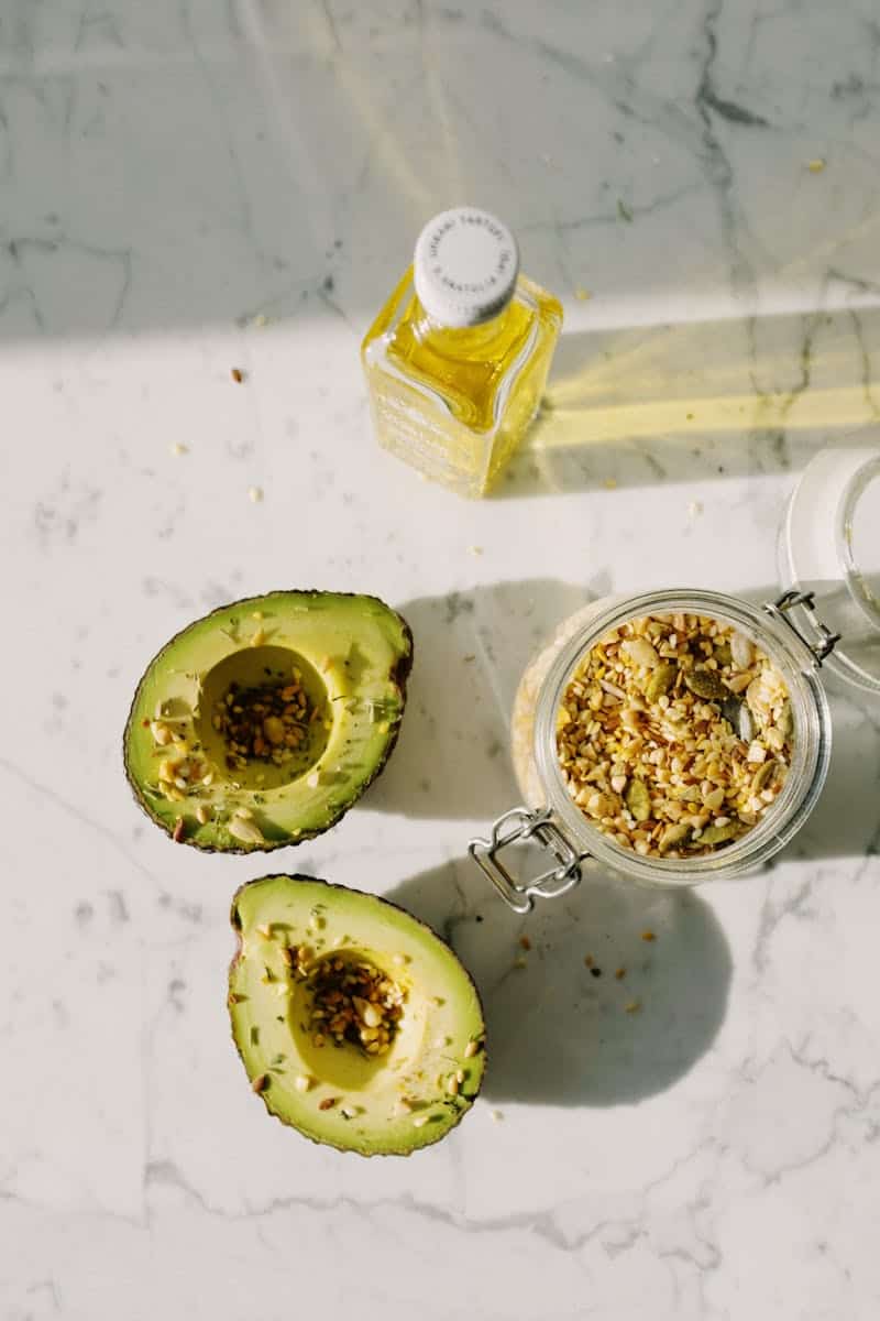 Fresh avocado halves with seeds and olive oil on marble surface, perfect for a keto diet.