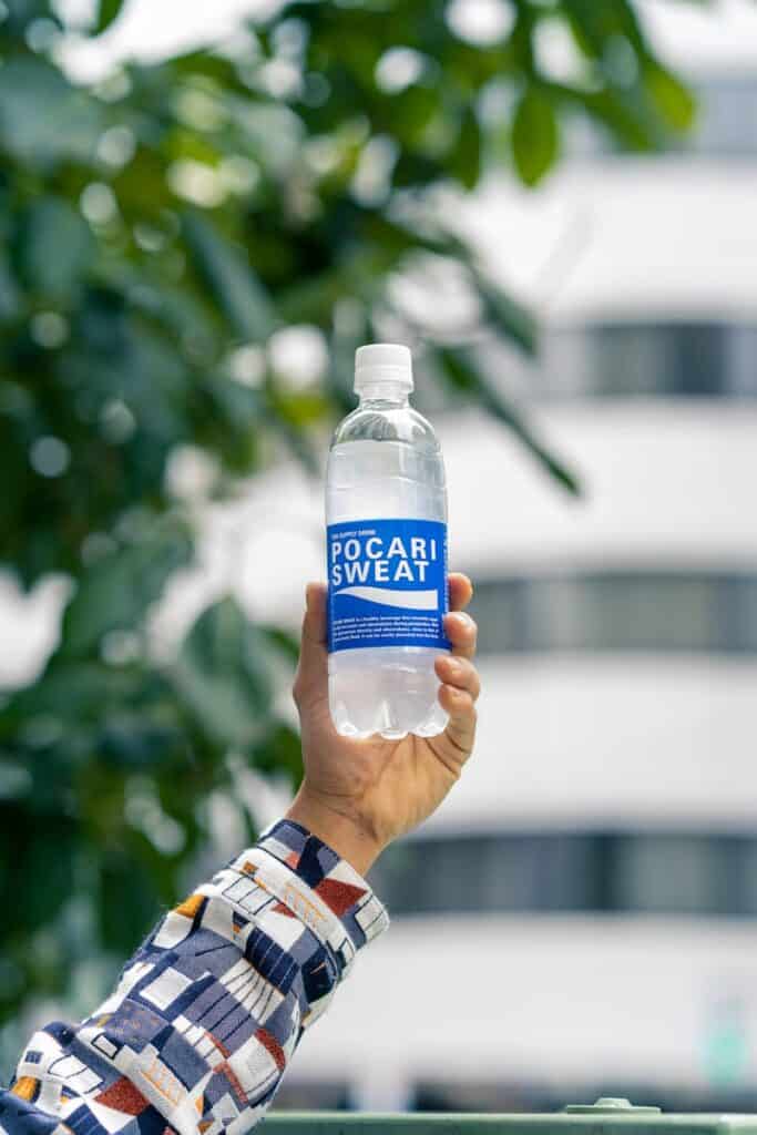 A hand holding a Pocari Sweat bottle outdoors in Tokyo, Japan, with blurred urban background.