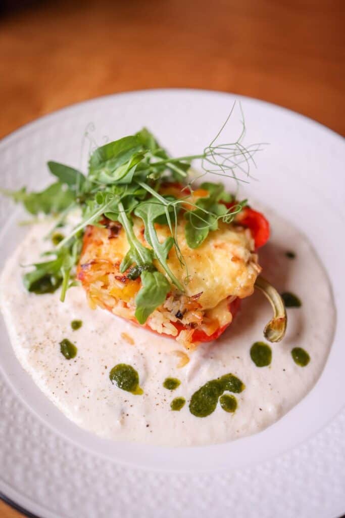 Delectable stuffed bell pepper topped with greens, served on a creamy sauce.