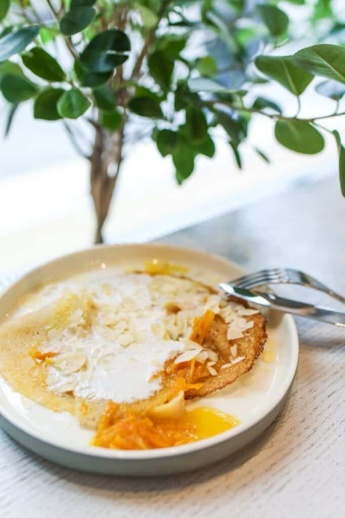 Crispy pancake topped with coconut flakes, fruit, and cream on a plate.