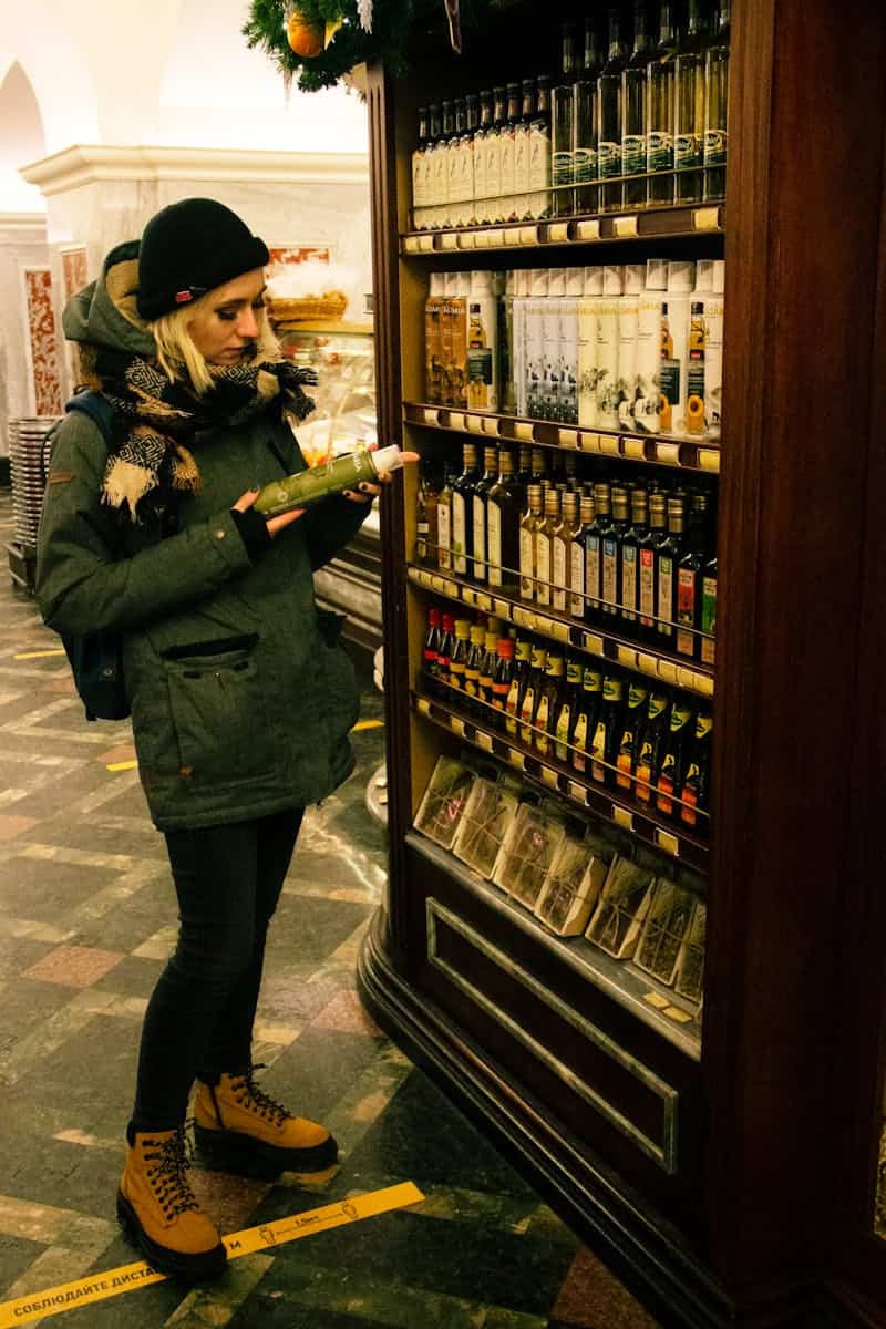 Adult woman shopping for groceries in a Russian store aisle, reading product labels.