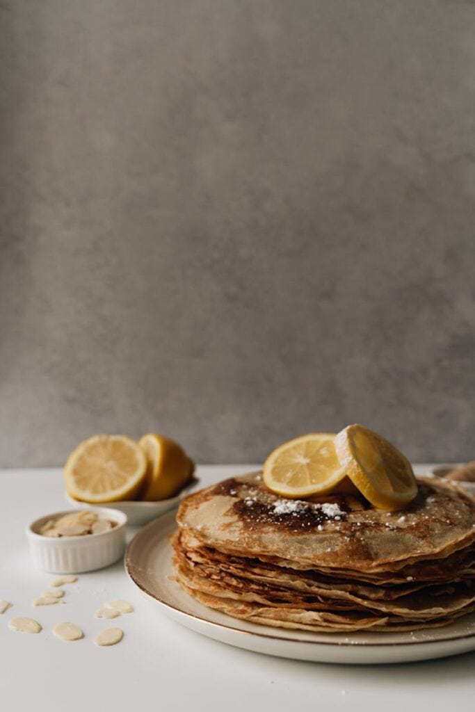 Stack of golden pancakes topped with lemon slices and almonds on a plate.