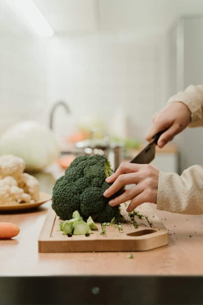 Close-up of hands slicing fresh organic broccoli on a kitchen counter, perfect for food preparation themes.