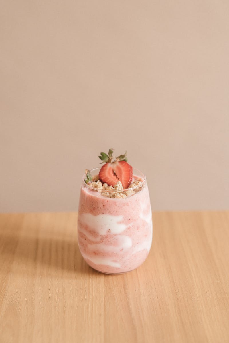 Delicious strawberry smoothie with granola topping in a glass on a wooden table.